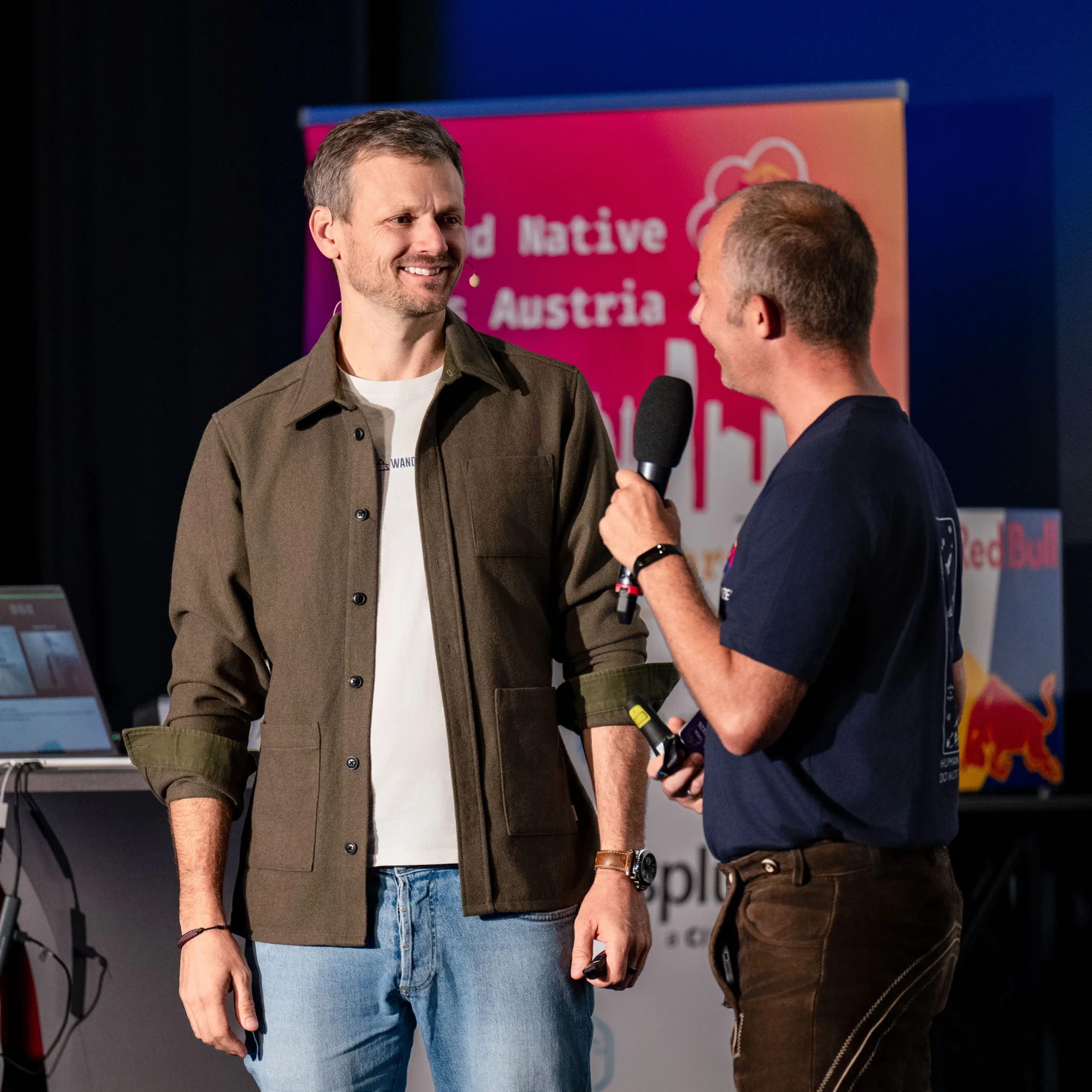 Two speakers chatting on stage in front of the conference banner